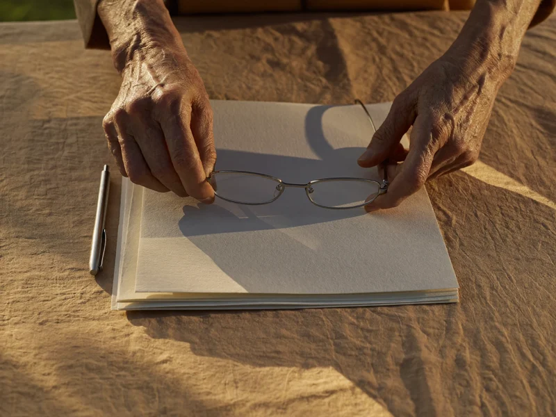 Mani anziane con occhiali da lettura su cartelle di carta vuote e senza scritte.